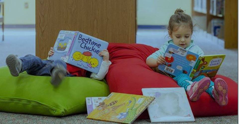 Two children read books on bean bag chairs