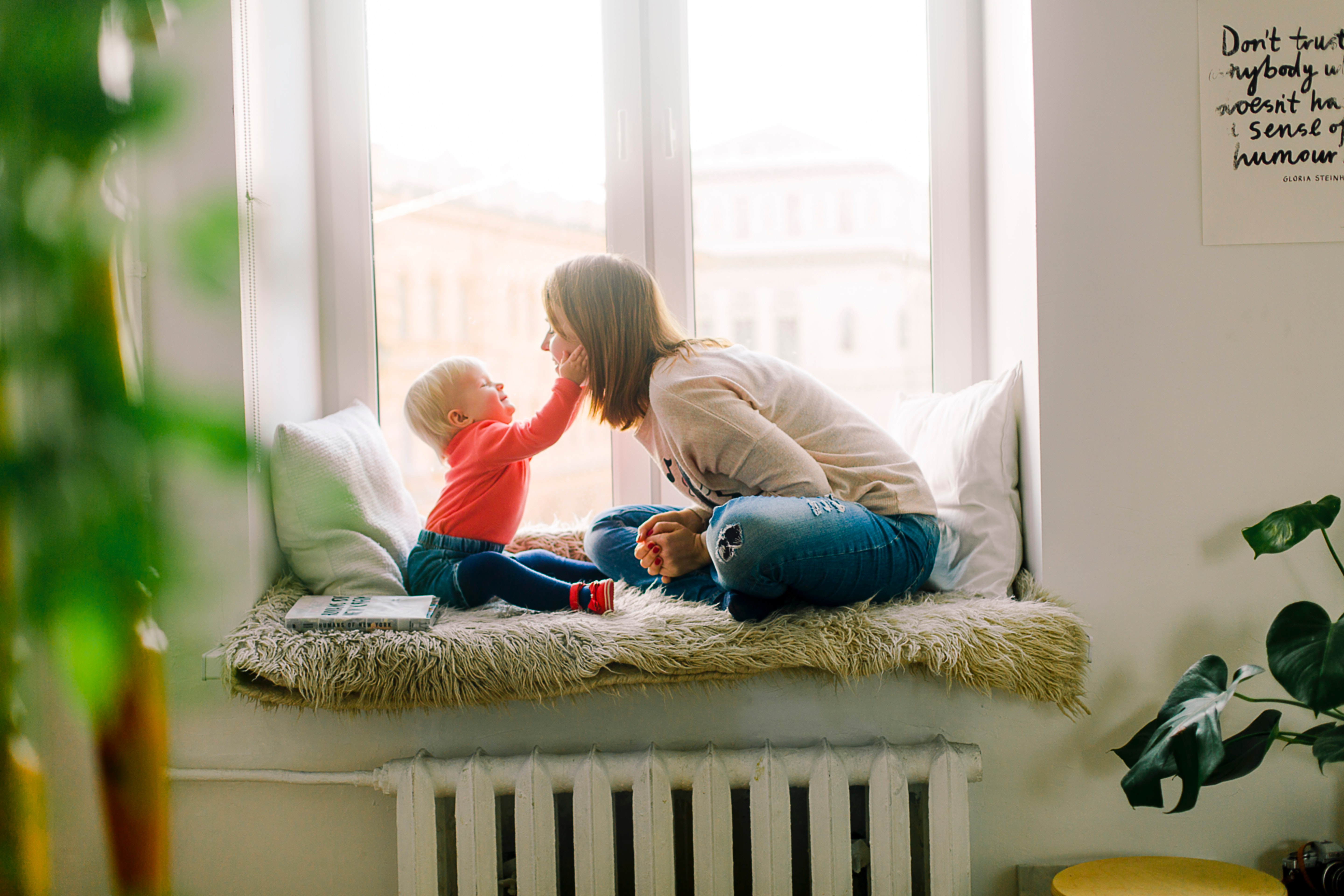 A baby reaches out for a woman's face in an affectionate gesture on the bay window seat
