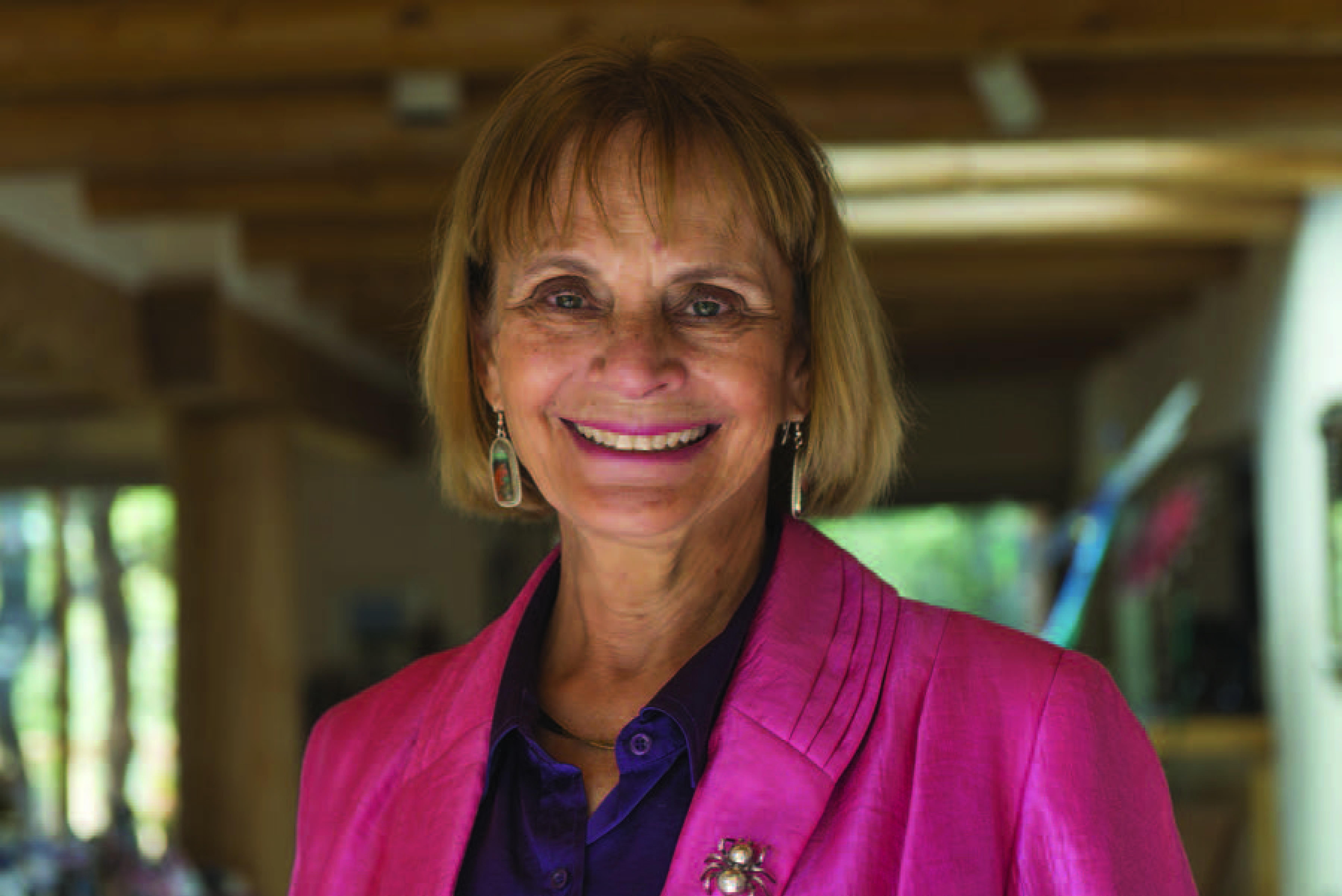 A woman with cropped blonde hair and a pink blazer smiles at the camera