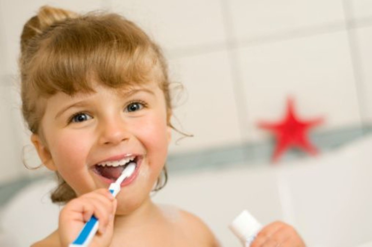 A young girl with blonde hair brushes her teeth with a blue and white toothbrush