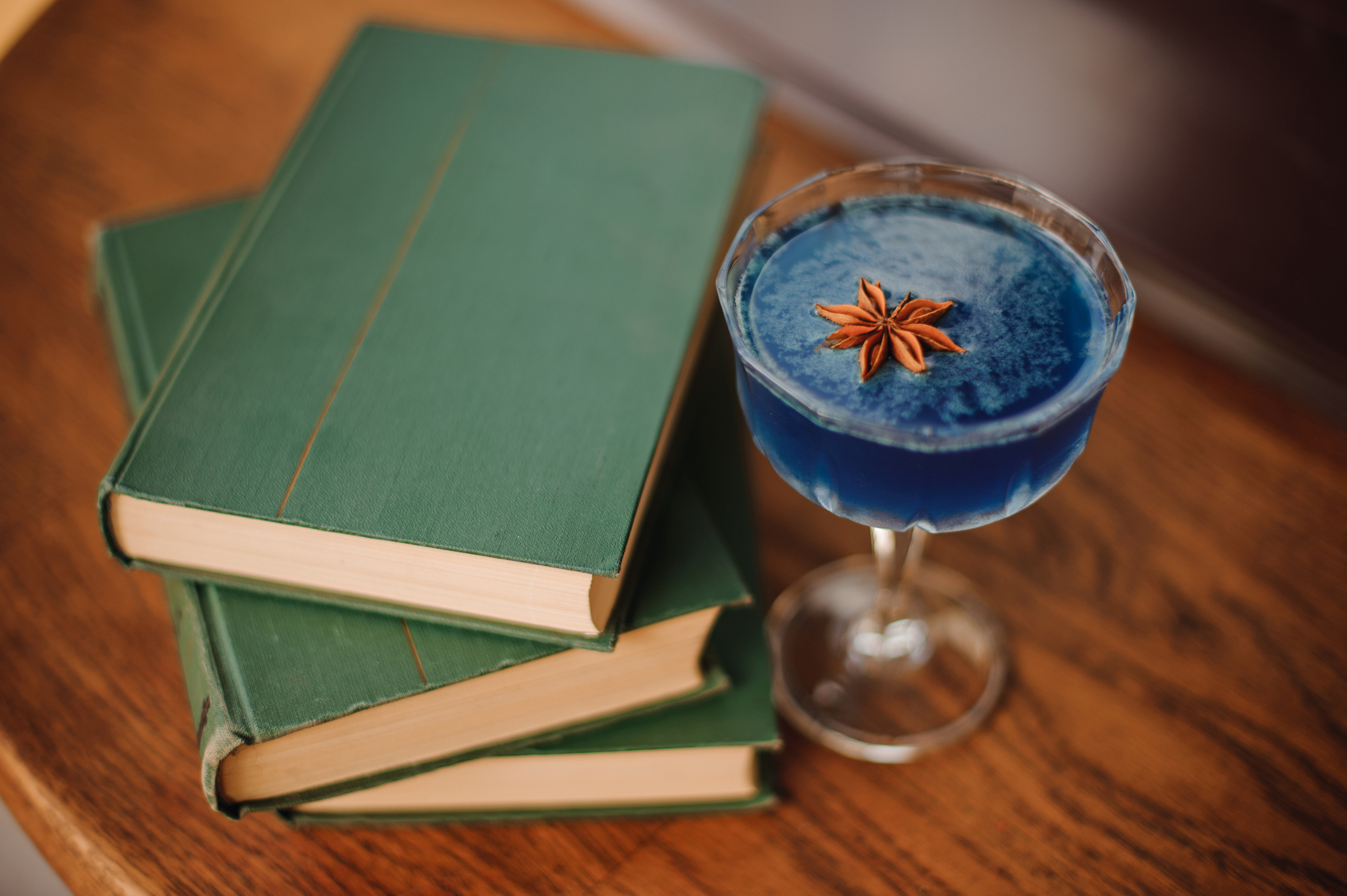 Blue cocktail with Star Anise on bar next to books