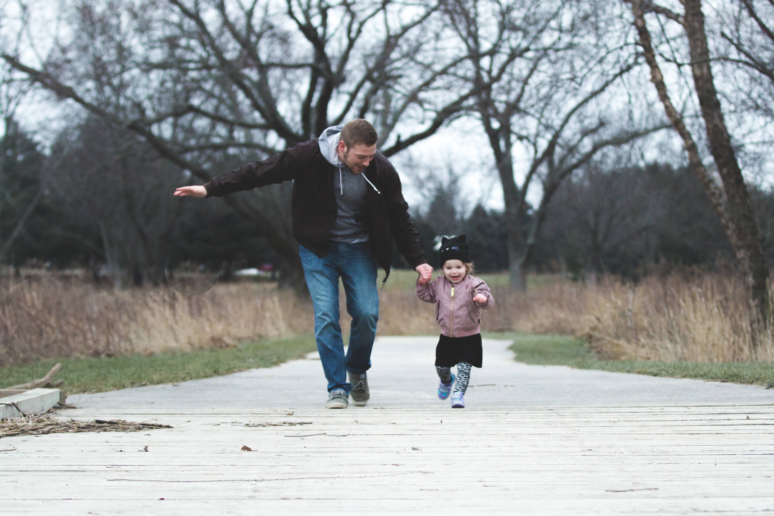 A man walks with a small female child down a pier