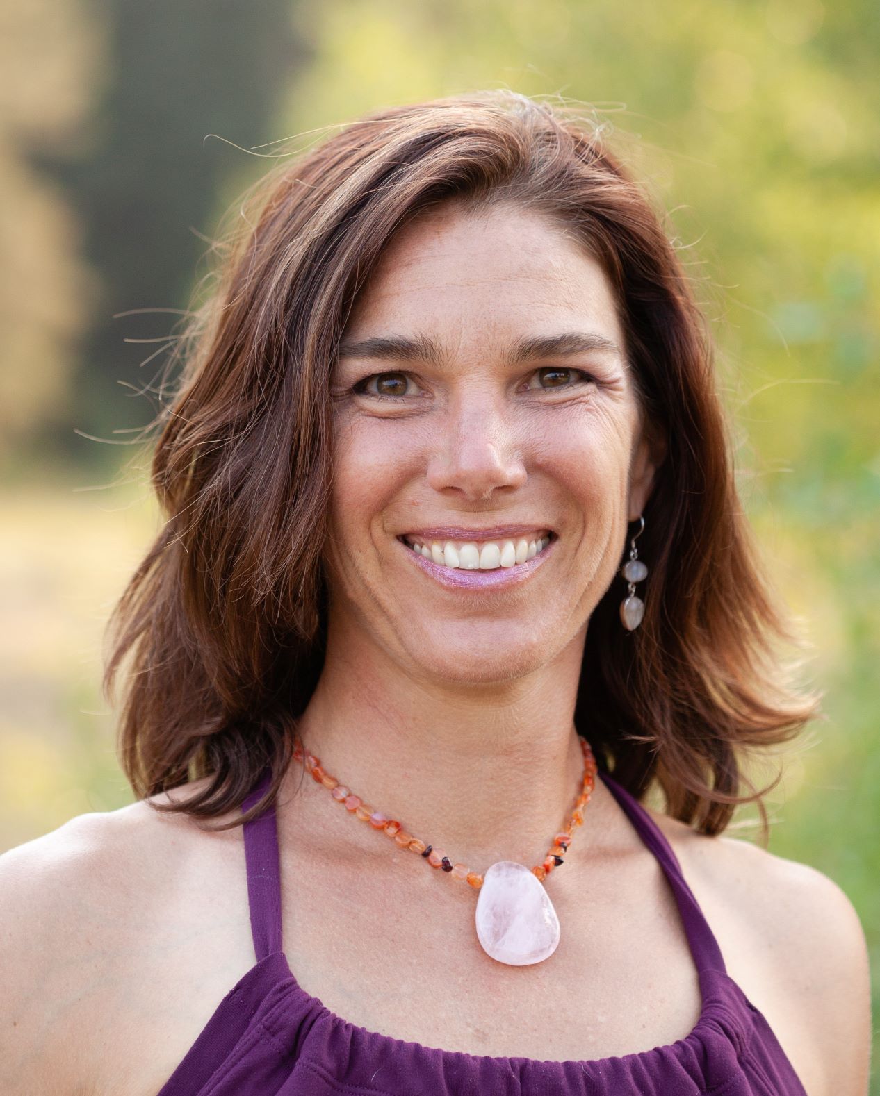 A woman with shoulder length brown hair and a purple dress smiles at the camera