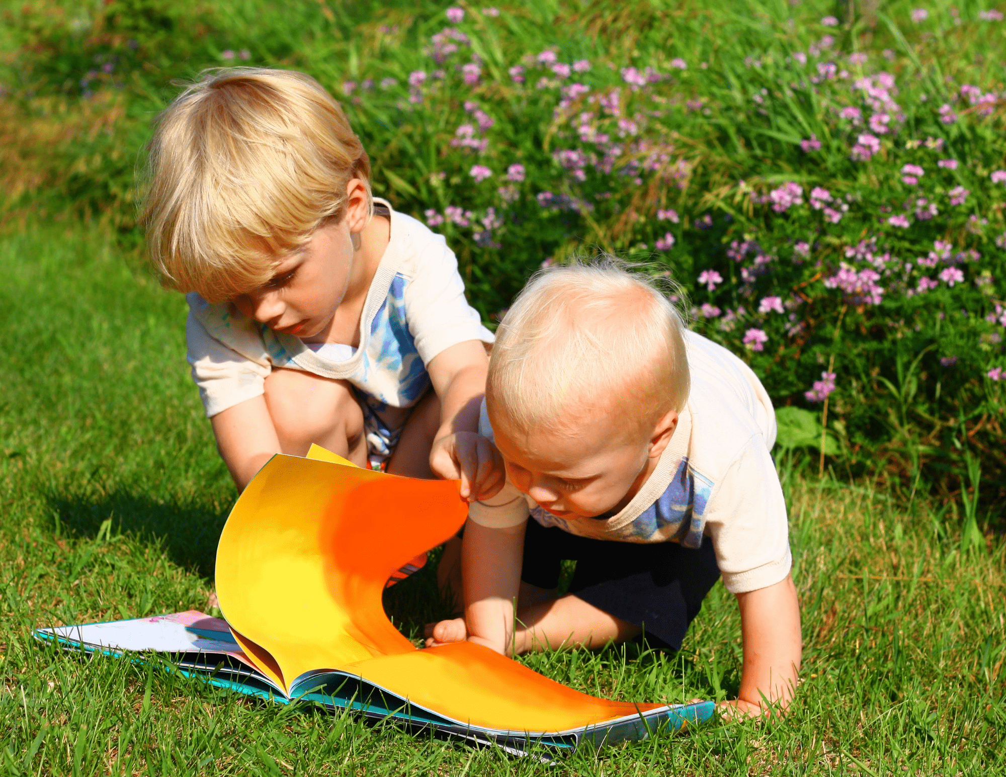 two children with blonde hair read a book outside